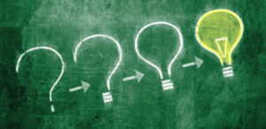 Una lavagna con dei punti di domanda che si trasformano in lampadine simbolo di innovazione