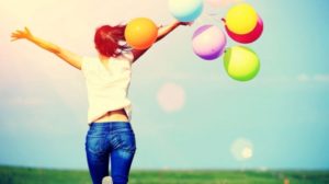 Una ragazza di spalle che esulta in un prato tra un volo di palloncini colorati