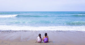 Due sorelline contemplano insieme il mare sedute a riva