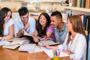 Un gruppo di studenti universitari sorridenti seduti al tavolo della biblioteca studiano insieme