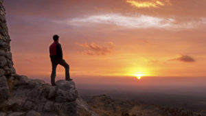 Un uomo sopra una roccia guarda il tramonto all'orizzonte