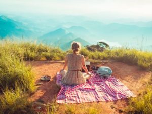 Una ragazza seduta sulla tovaglia da picnic di spalle guarda il panorama di montagne davante a sé