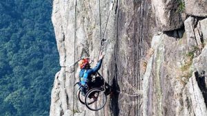 Un uomo che scala una parete di montagna verticale essendo in carrozzina perché disabile