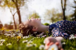 Una ragazza stesa su un prato fiorito guarda il cielo azzurro sopra di lei