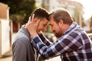 Un padre stringe tra le mani la testa e il viso del figlio giovane adulto per infondergli felicità e vitalità