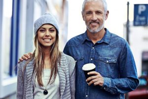 Un padre per strada sorridente con la sua figlia ormai grande le posa la mano sulla spalla come per sostenerla nelle scelte importanti