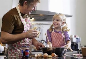 Un padre con la sua bambina cucinano sorridenti 