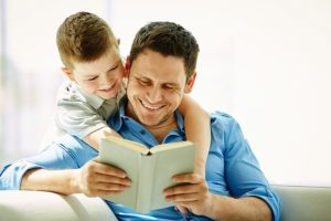 Un papà felice di leggere un libro al proprio bambino che lo ascolta interessato abbracciandolo