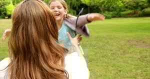 Una bambina che corre incontro alla mamma che l'aspetta a braccia aperte seduta sul prato