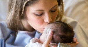 Una mamma bacia tenerissima la testa del suo bambino appena nato, ancora in sala parto