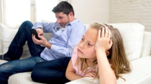 Un padre sul divano guarda lo smartphone e non la sua bambina