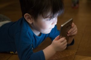 Un bambino che si morde le labbra troppo intento a guardare uno smartphone col viso illuminato dalla luce blu