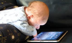 Un neonato riverso su un Ipad con gli occhi spalancati sulla luce blu del touchscreen