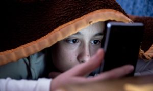 Un preadolescente con lo smartphone sotto le coperte al posto di dormire