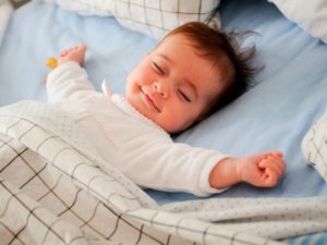Un bambino molto piccolo dorme a pancia in su sorridente e a braccia aperte 