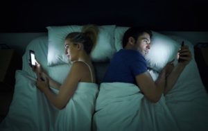 Un uomo e una donna a letto si voltano le spalle e si isolano ciascuno con il proprio smartphone