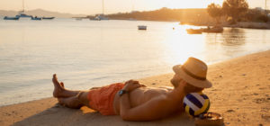 Un giovane uomo fa un riposino in riva al mare al tramonto col cappello di paglia sugli occhi