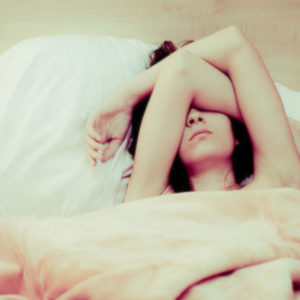 Una giovane donna a letto fatica a dormire e incrocia le braccia sul viso per riuscire a riposare