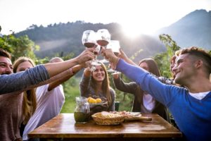 Un gruppo di amici brindano con calici di vino rosso a tavola e sullo sfondo colline