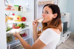 Una giovane donna apre il frigo e mangia la prima cosa che le capita a tiro guardando di non essere scoperta