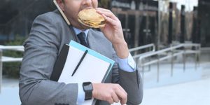 Un uomo stressato dal lavoro mangia di corsa un panino appena fuori dall'ufficio