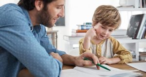 Un papà sorridente aiuta nei compiti delle vacanze il suo bambino seduto al tavolo in cucina