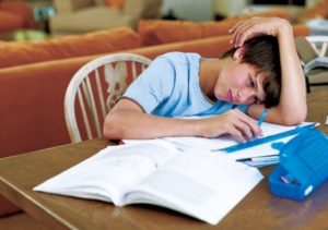 Un ragazzo con la testa reclinata sui compiti delle vacanze studia malvolentieri