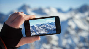 Una mano regge uno smartphone con cui sta fotografando un bellissimo panorama di montagne