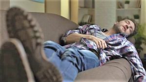 Un giovane uomo ozia e dorme in divano senza riposare bene