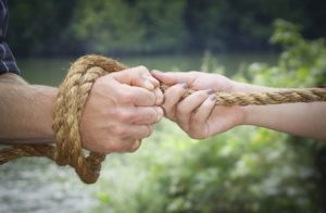 Una mano maschile legata con una corda e tirata o trattenuta da una mano femminile