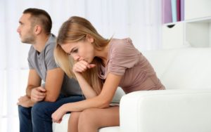 Una giovane donna seduta sul divano riflette combattuta sul da farsi mentre il suo uomo è distratto e distante