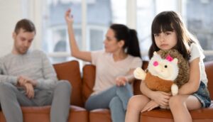 Una bambina col suo peluche in braccio e lo sguardo assente è presente al litigio dei suoi genitori seduti sul divano e con un'alta conflittualità da prevenire
