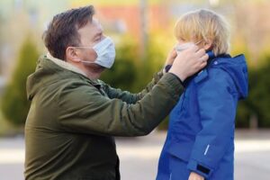 Un papà all'aperto con mascherina sistema la mascherina del suo bambino