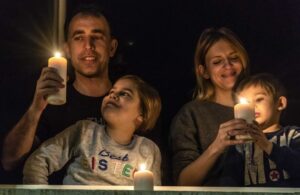 Papà mamma figlio e figlia alla finestra al buio e con le candele accese durante il lockdown