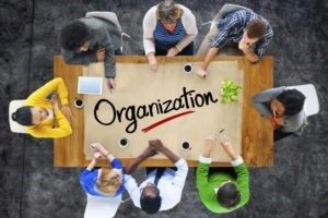 Dall'alto un gruppo di persone al lavoro su un tavolo con la grande scritta Organization