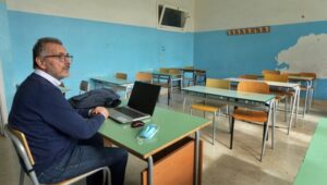 Un professore in aula da solo con computer mascherina e banchi vuoti