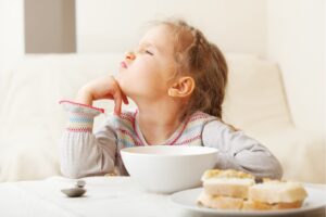 Una bambina seduta a tavola davanti alla sua tazza avanza pretese capricciose