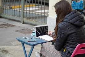 Una ragazza stanca della dad segue le lezioni con computer e tavolino fuori dalla scuola