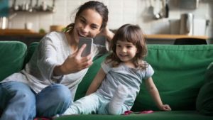 Una mamma seduta sul divano si fa un selfie con la sua bambina facendo sharenting