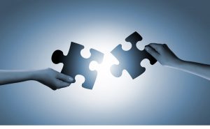 Su sfondo di luce due mani combinano un puzzle simbolo dei neuroni specchio e della sensibilità