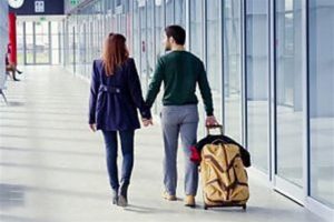 Una giovane coppia per mano e di spalle cammina all'aeroporto trascinando una grossa valigia pronti per realizzare i loro sogni