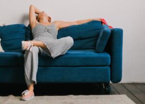 Una giovane donna in tuta stesa sul divano di casa a causa della stanchezza di primavera