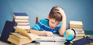 Un ragazzino con le mani tra i capelli legge sommerso dai libri e dai compiti
