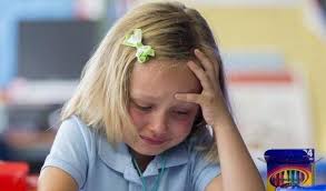 Una bambina piccola e bionda piange sopra i quaderni di scuola